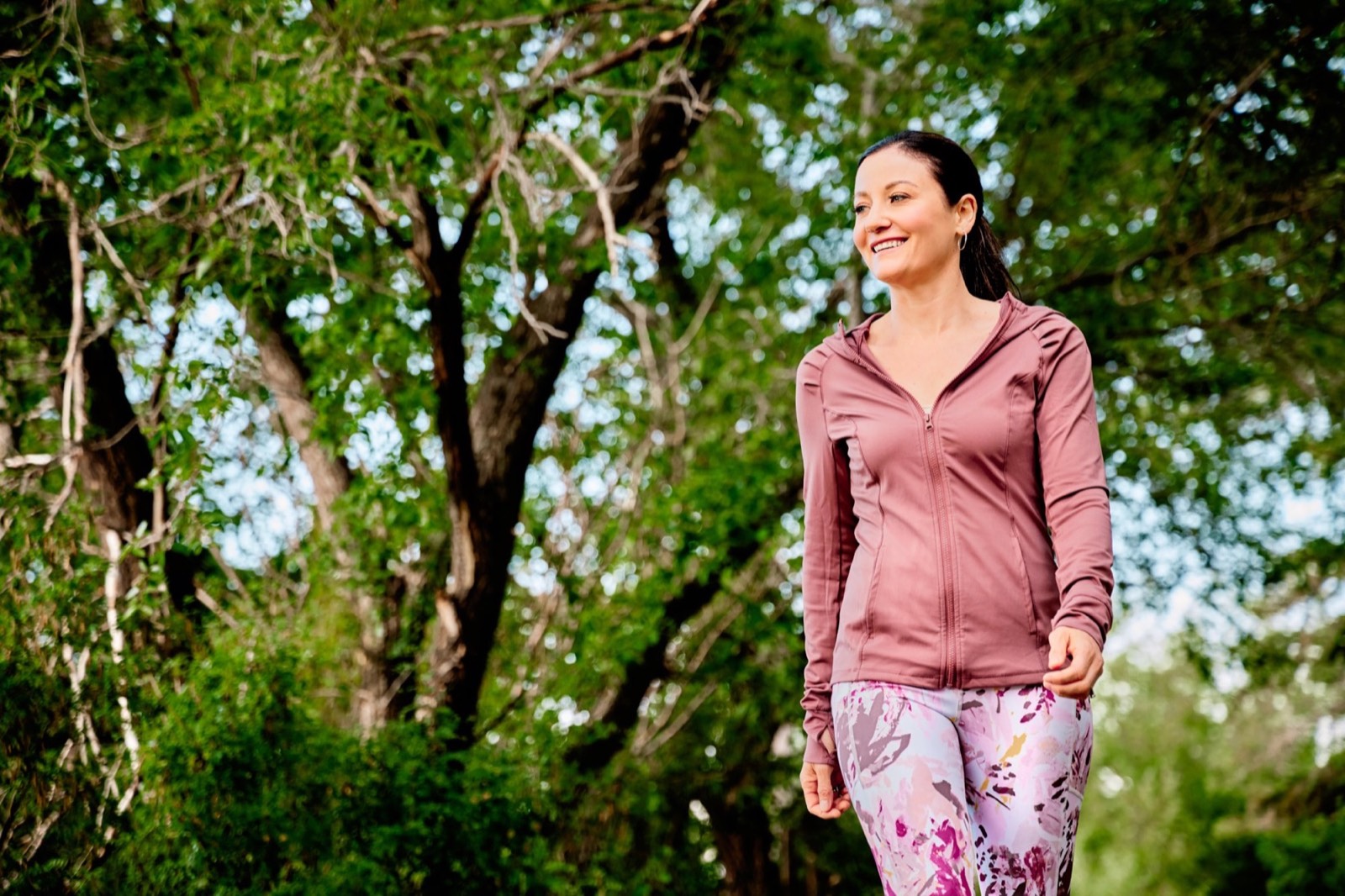 April walking outdoors under green trees, smiling
